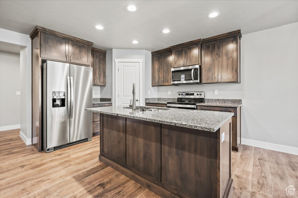 Kitchen with light hardwood / wood-style floors, a kitchen island with sink, dark brown cabinets, sink, and stainless steel appliances