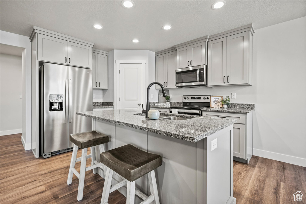 Kitchen featuring appliances with stainless steel finishes, light stone counters, a kitchen island with sink, and hardwood / wood-style floors