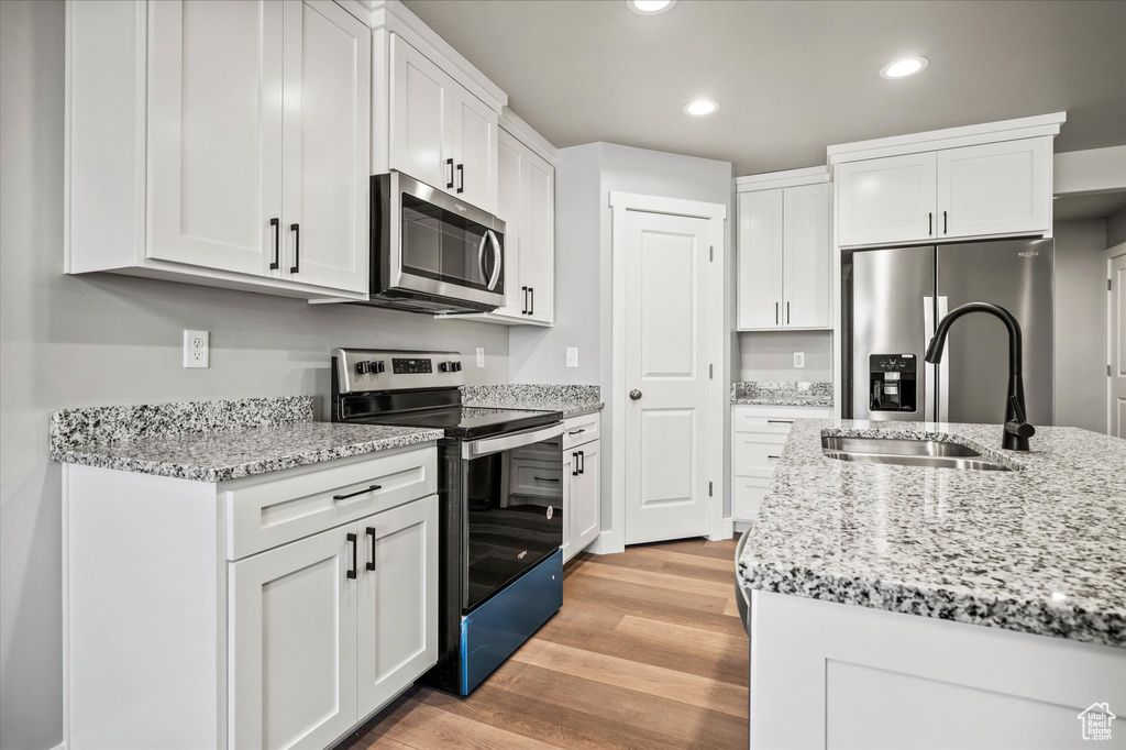 Kitchen featuring light stone counters, sink, white cabinetry, light hardwood / wood-style flooring, and appliances with stainless steel finishes