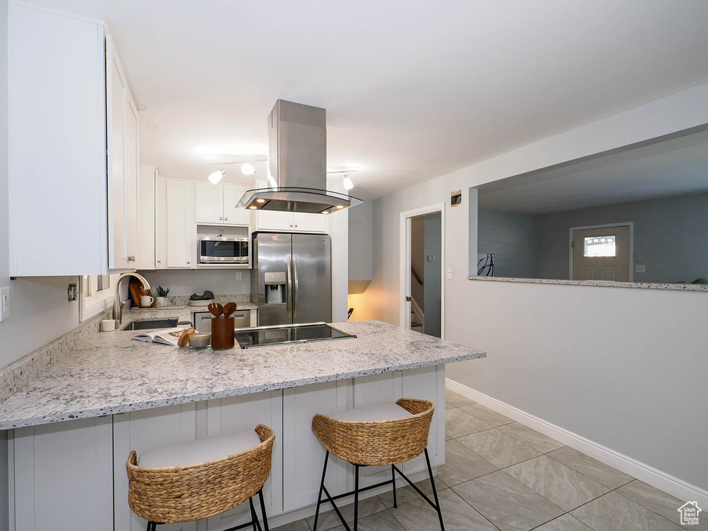 Kitchen featuring white cabinets, kitchen peninsula, island exhaust hood, appliances with stainless steel finishes, and a breakfast bar area