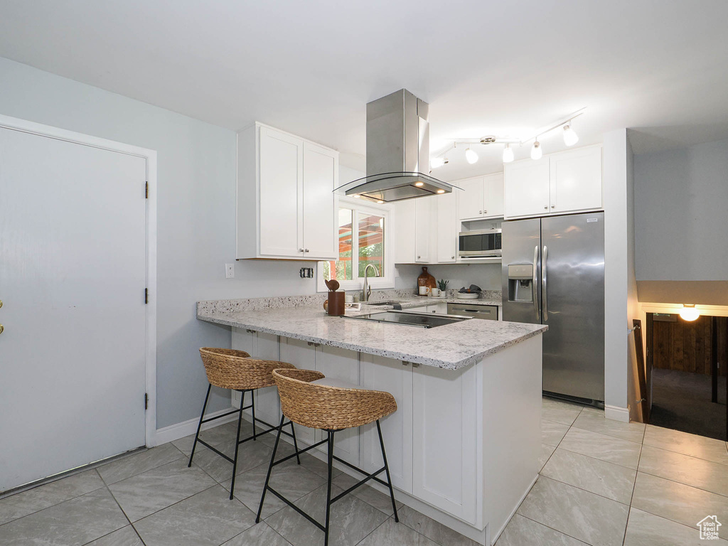 Kitchen with stainless steel appliances, a breakfast bar, kitchen peninsula, island range hood, and white cabinetry