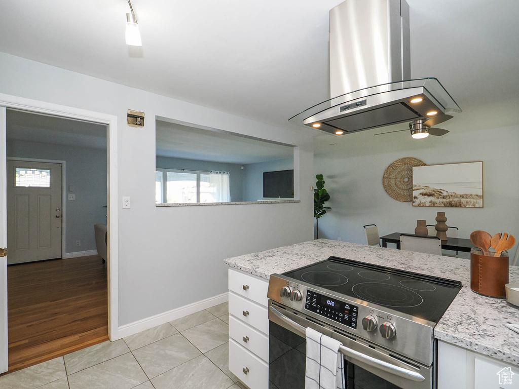 Kitchen with light stone counters, light hardwood / wood-style floors, high end range, white cabinetry, and island exhaust hood