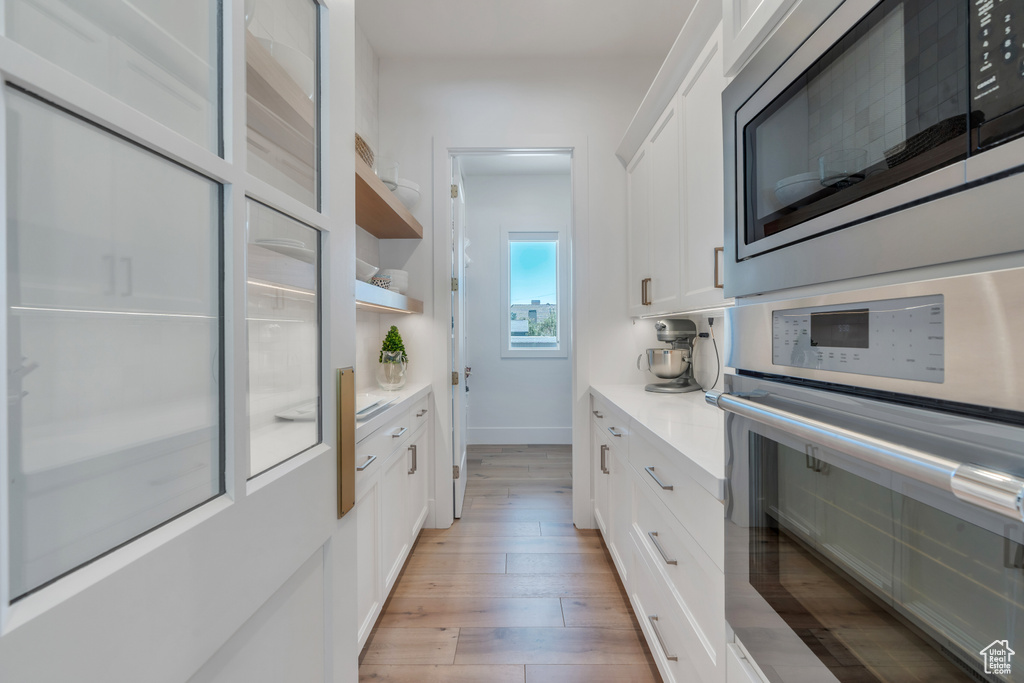 Kitchen with light hardwood / wood-style flooring, stainless steel appliances, and white cabinets