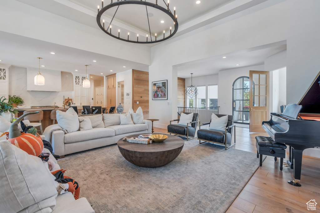 Living room with a notable chandelier, light hardwood / wood-style flooring, a towering ceiling, and a raised ceiling