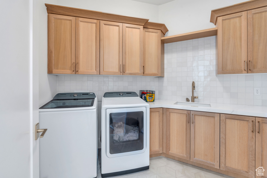 Clothes washing area with cabinets, sink, and washer and dryer