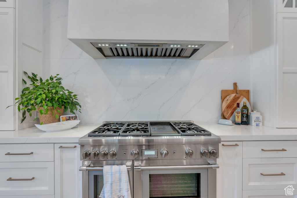 Kitchen with range with two ovens, backsplash, white cabinetry, and range hood