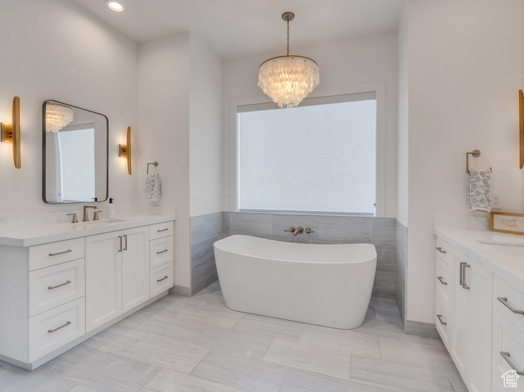 Bathroom with vanity, tile walls, a chandelier, and a tub