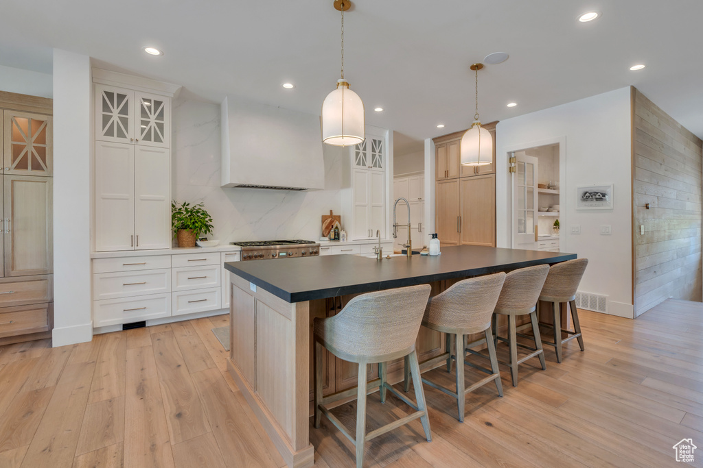 Kitchen with white cabinetry, pendant lighting, light hardwood / wood-style flooring, a center island with sink, and sink