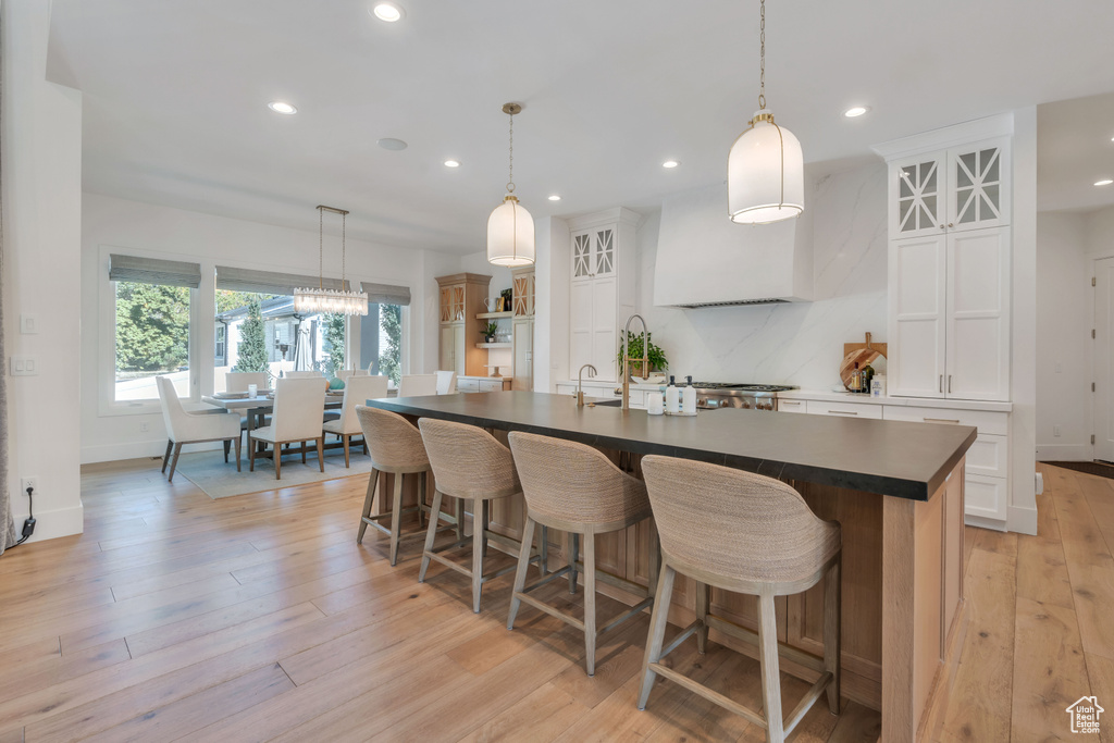 Kitchen featuring a spacious island, white cabinets, decorative light fixtures, and light hardwood / wood-style flooring