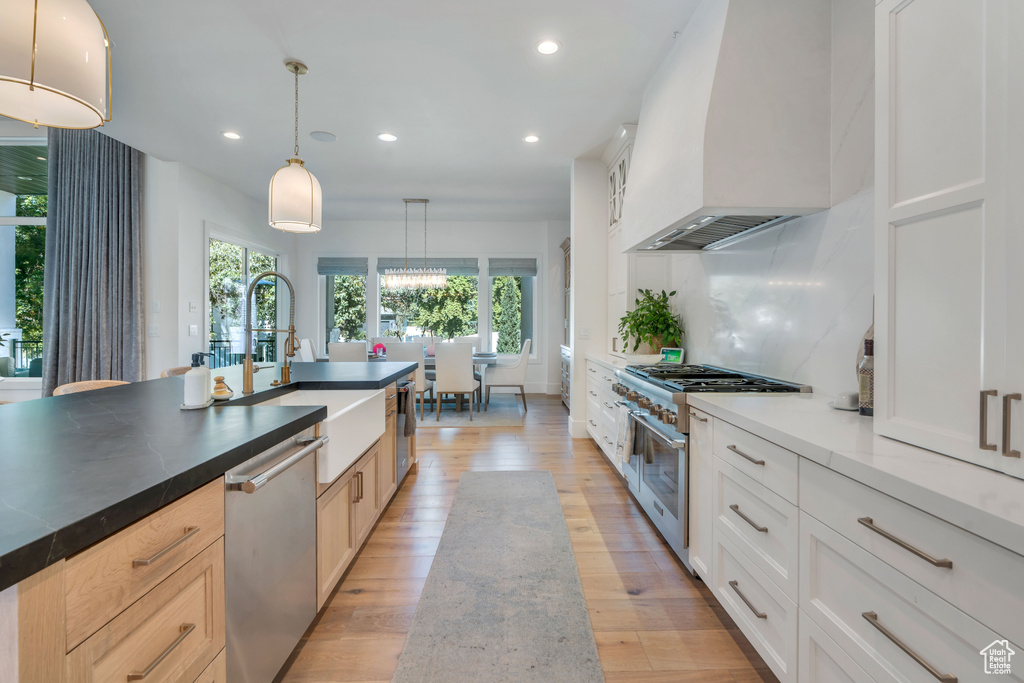 Kitchen with appliances with stainless steel finishes, wall chimney exhaust hood, light wood-type flooring, and decorative light fixtures