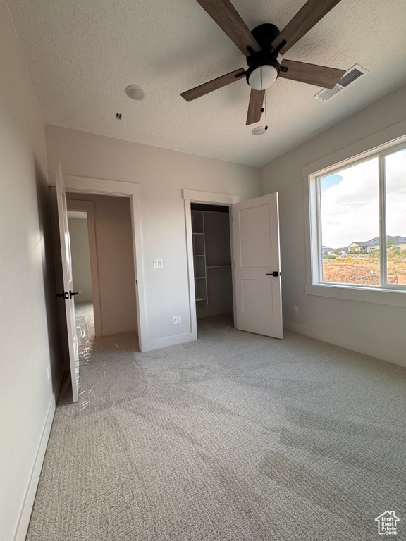 Unfurnished bedroom featuring a closet, light carpet, a textured ceiling, and ceiling fan