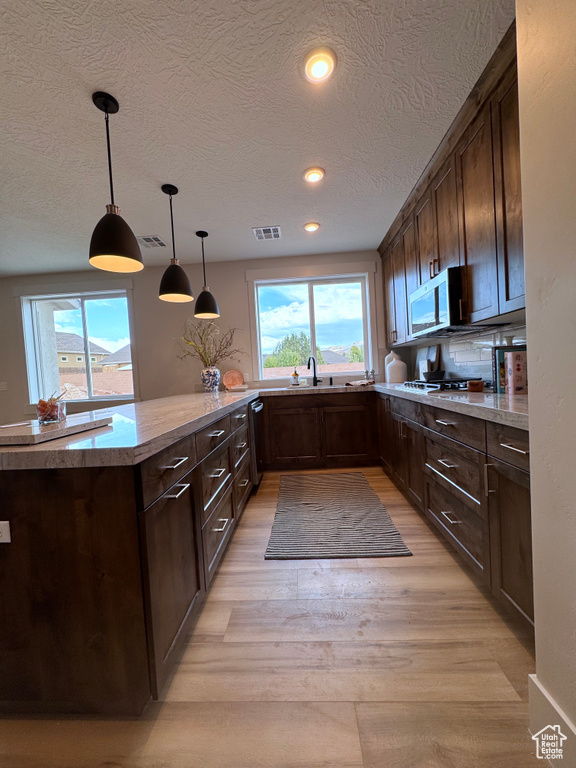 Kitchen featuring hanging light fixtures, sink, dark brown cabinets, a textured ceiling, and light wood-type flooring