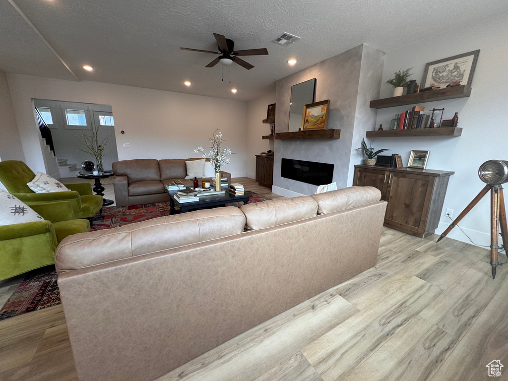 Living room featuring ceiling fan, a textured ceiling, and light wood-type flooring