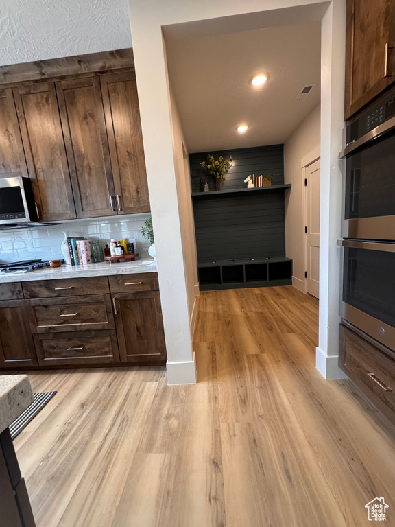 Kitchen featuring appliances with stainless steel finishes, dark brown cabinets, light hardwood / wood-style flooring, and backsplash