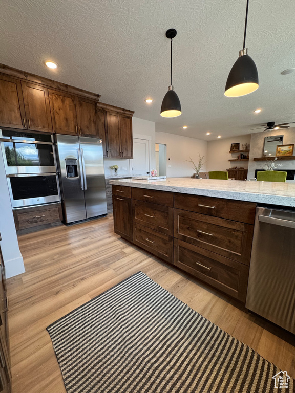 Kitchen with appliances with stainless steel finishes, decorative light fixtures, light hardwood / wood-style floors, and a textured ceiling