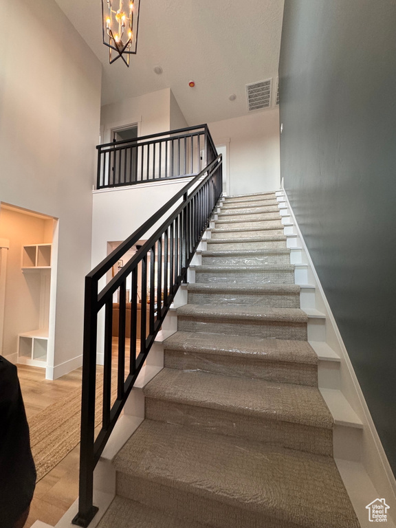 Stairs featuring a towering ceiling, wood-type flooring, and an inviting chandelier