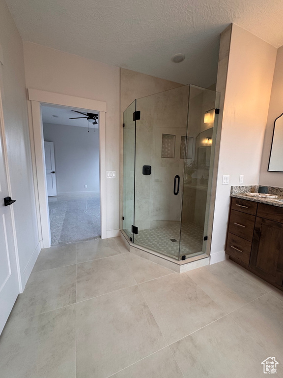 Bathroom featuring ceiling fan, vanity, tile patterned flooring, a shower with shower door, and a textured ceiling