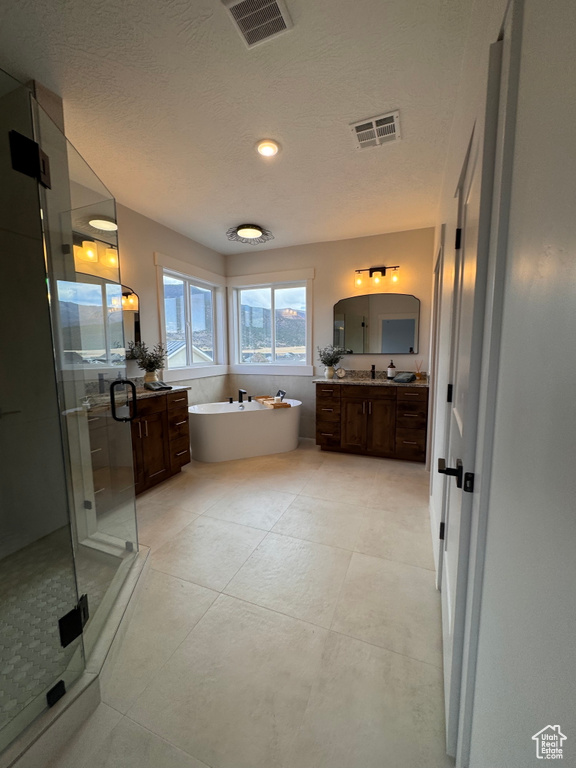 Bathroom with a textured ceiling, tile patterned floors, vanity, and shower with separate bathtub