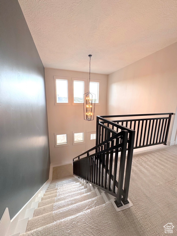 Stairs with carpet floors, a textured ceiling, and a chandelier