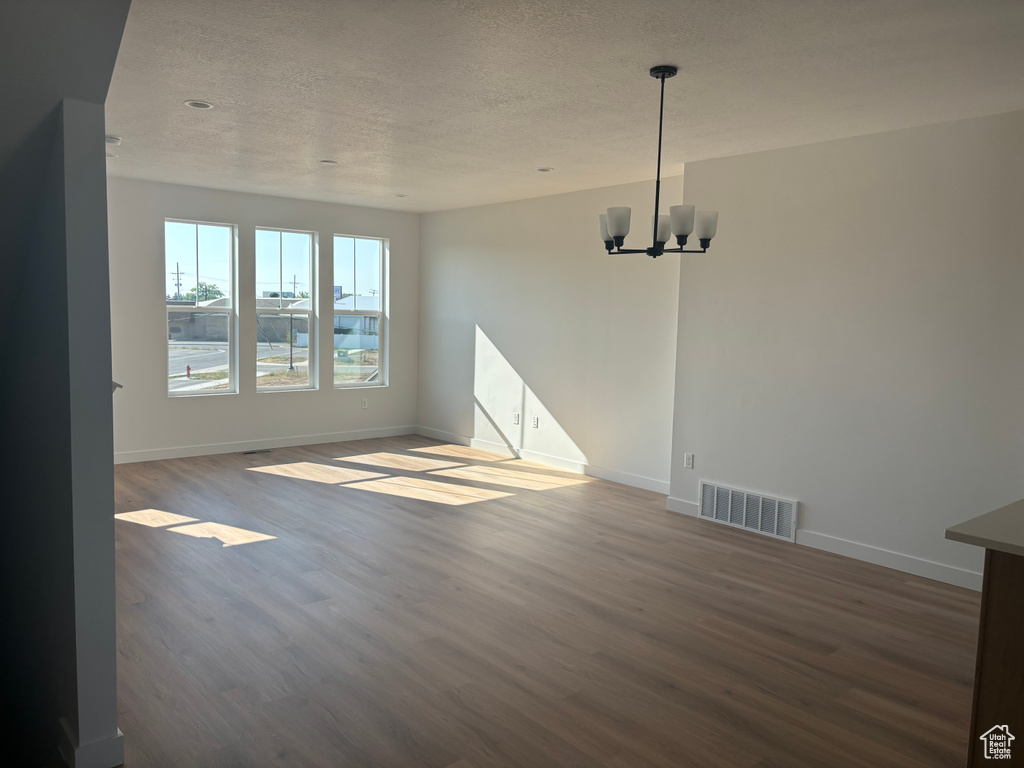 Spare room with wood-type flooring, a notable chandelier, and a textured ceiling