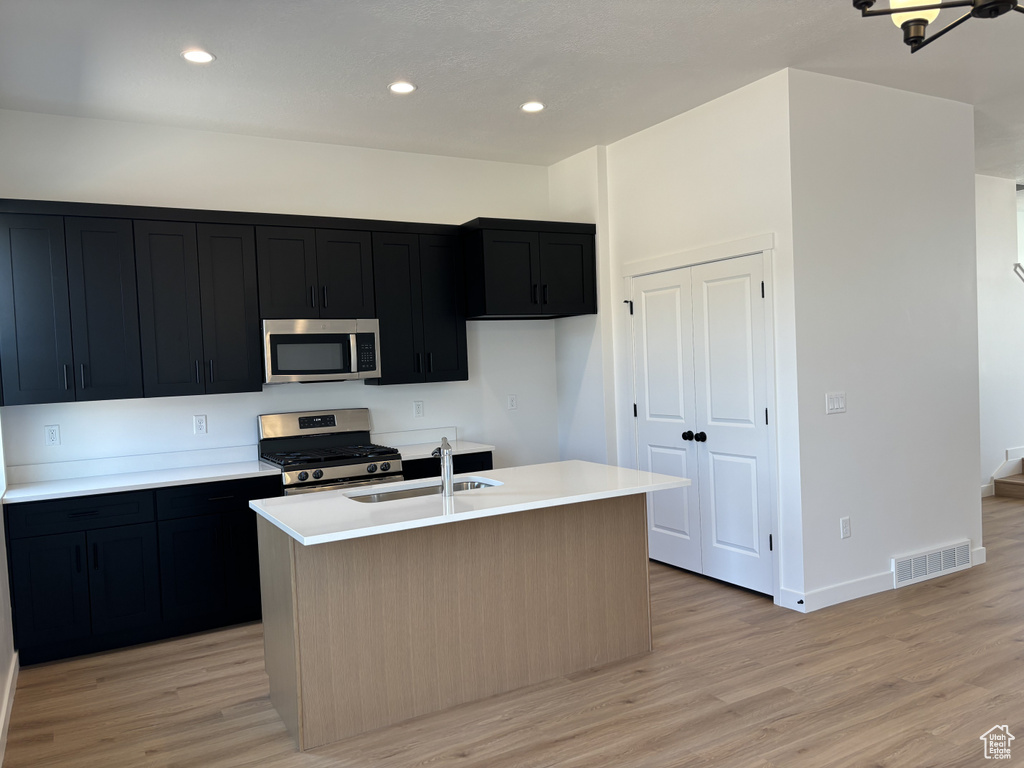 Kitchen with a center island with sink, appliances with stainless steel finishes, sink, and light wood-type flooring