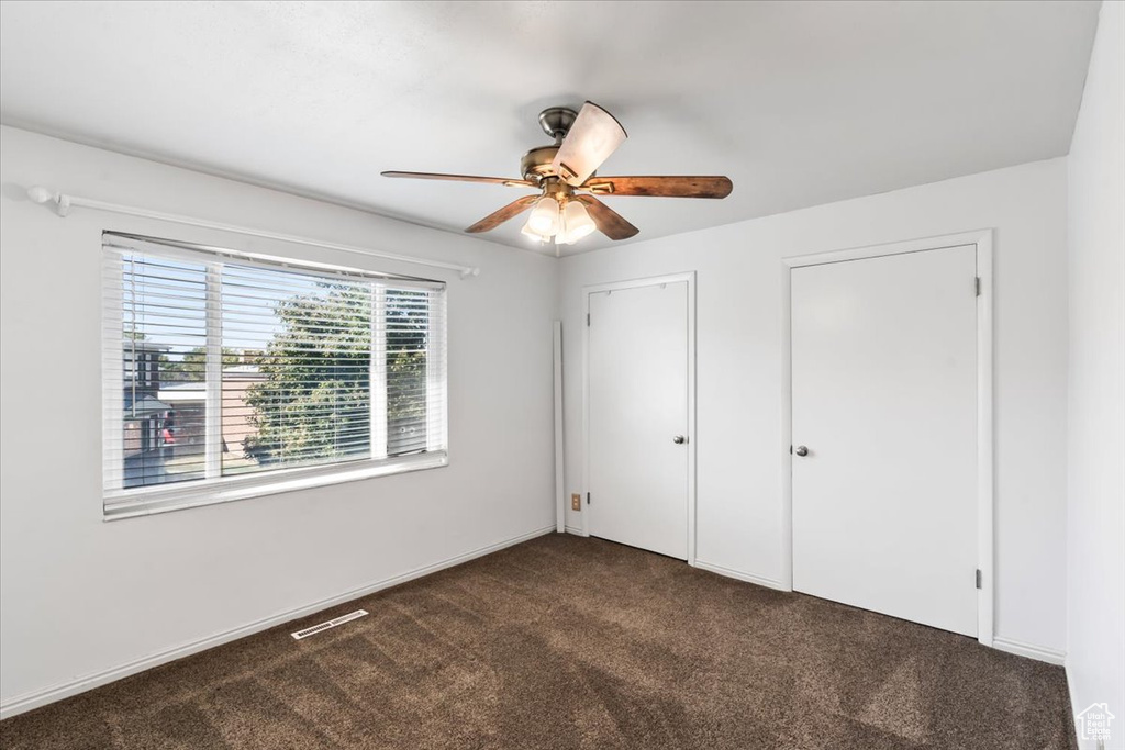 Unfurnished bedroom with dark carpet and ceiling fan