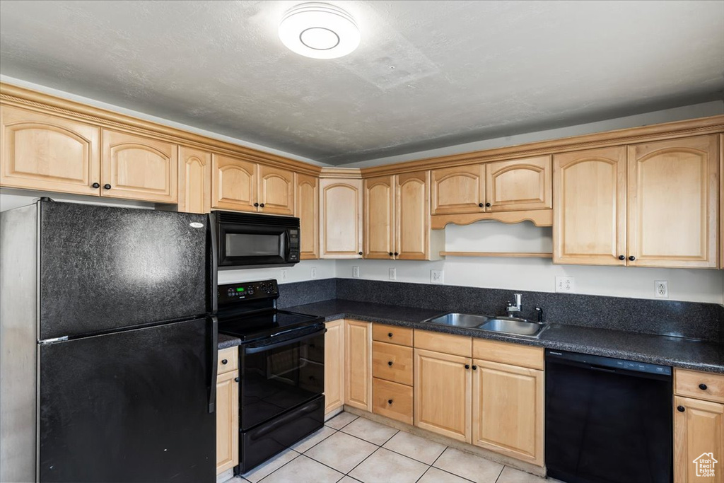 Kitchen featuring light tile patterned floors, light brown cabinets, sink, and black appliances