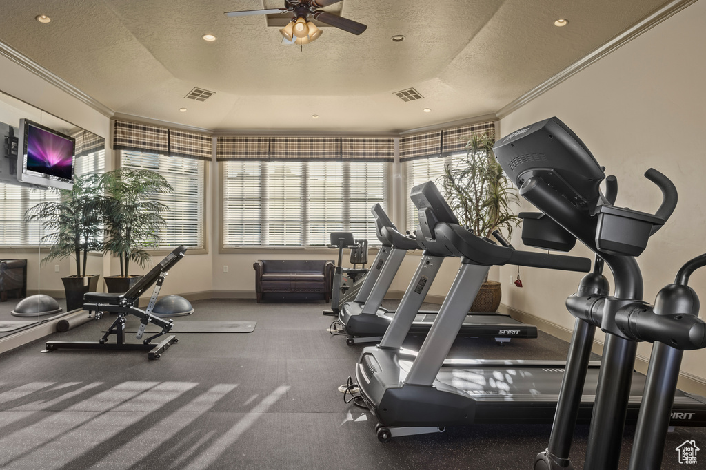 Gym with ceiling fan, a textured ceiling, a tray ceiling, and ornamental molding