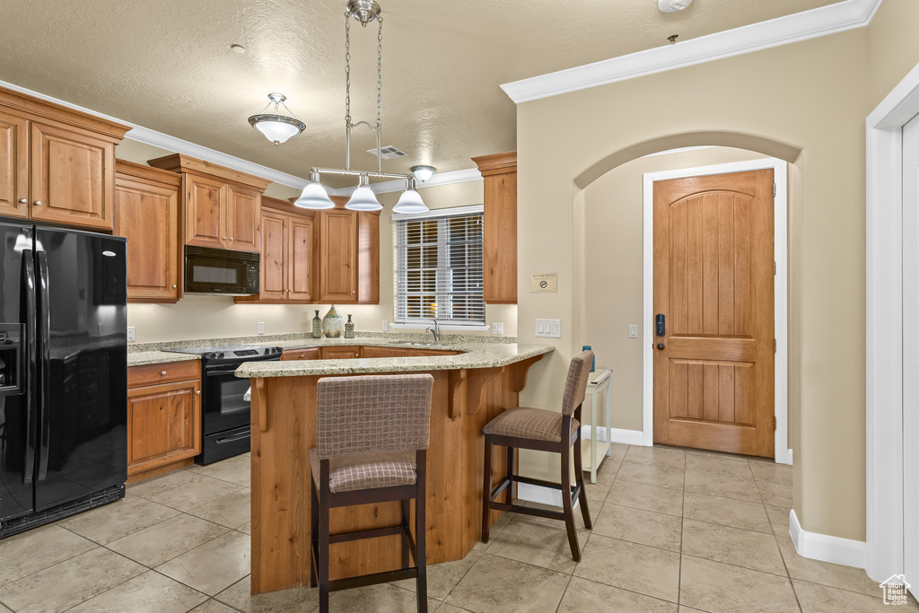 Kitchen with light stone counters, ornamental molding, kitchen peninsula, a textured ceiling, and black appliances