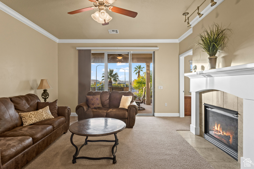 Living room with ceiling fan, light carpet, ornamental molding, and a tile fireplace