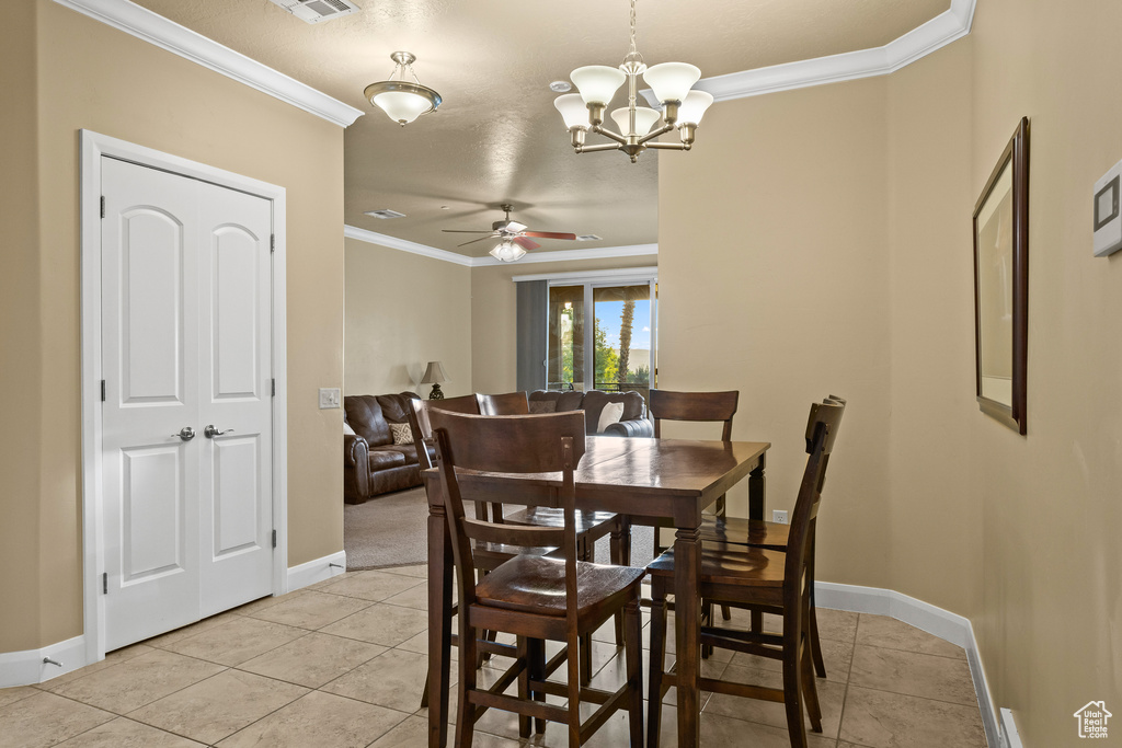 Tiled dining space with ornamental molding, a textured ceiling, and ceiling fan with notable chandelier