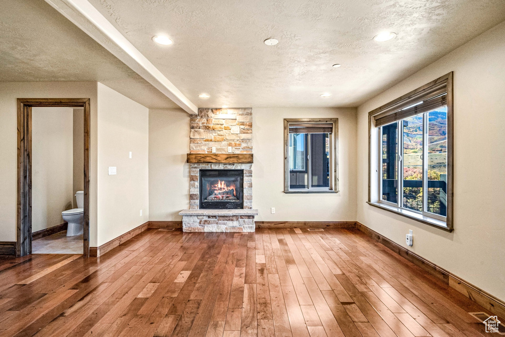 Unfurnished living room with a textured ceiling, a stone fireplace, and hardwood / wood-style flooring