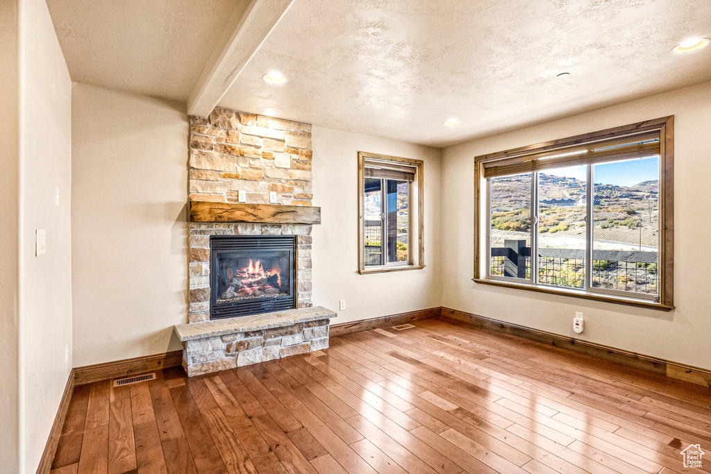 Unfurnished living room featuring wood-type flooring, beamed ceiling, a healthy amount of sunlight, and a stone fireplace