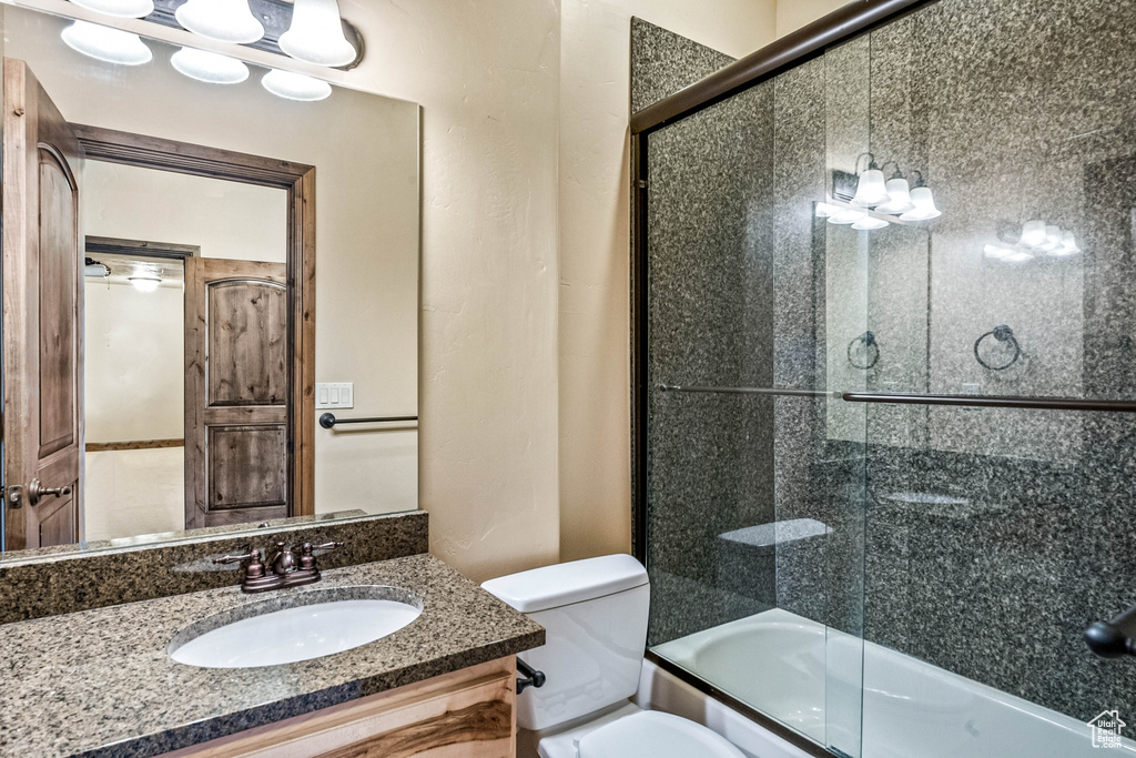 Full bathroom with enclosed tub / shower combo, vanity, and toilet