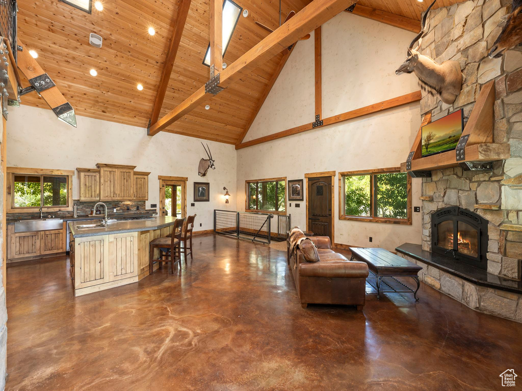 Living room featuring beam ceiling, wood ceiling, sink, a stone fireplace, and high vaulted ceiling