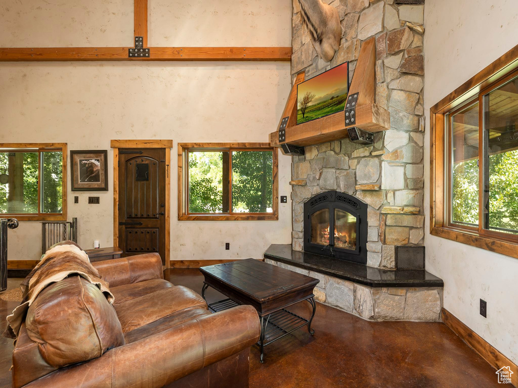 Living room featuring concrete floors, a stone fireplace, beamed ceiling, and a healthy amount of sunlight