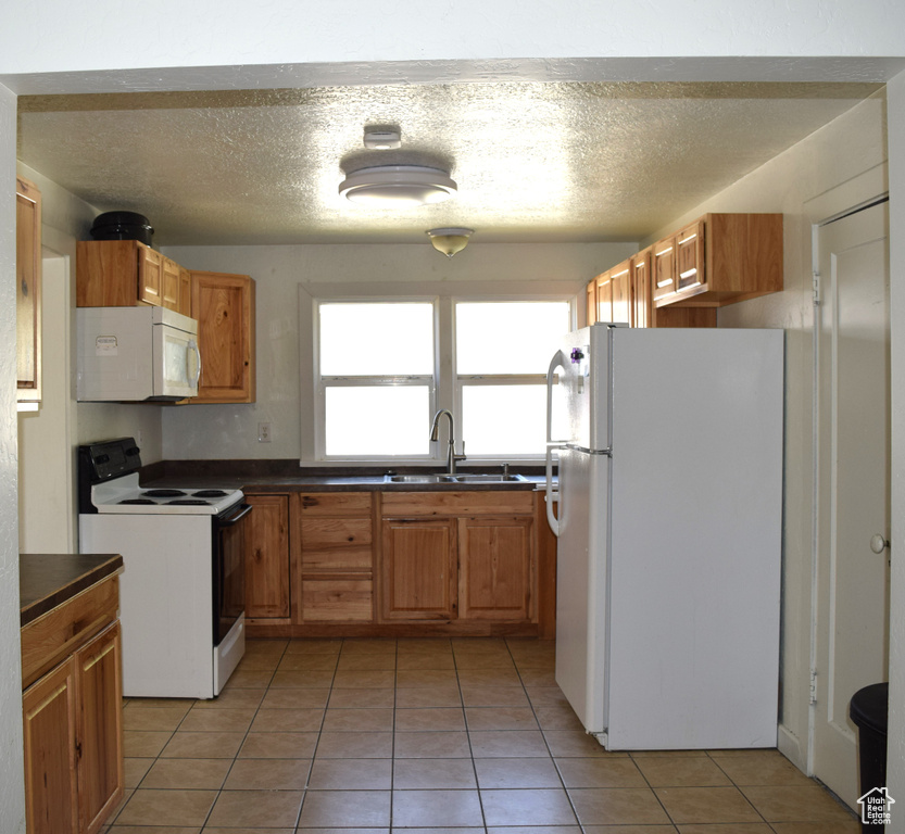 Kitchen with white appliances, sink, light tile patterned floors, and a textured ceiling