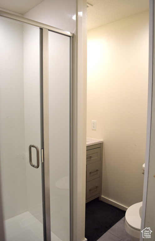 Bathroom featuring vanity, a shower with shower door, toilet, and tile patterned flooring