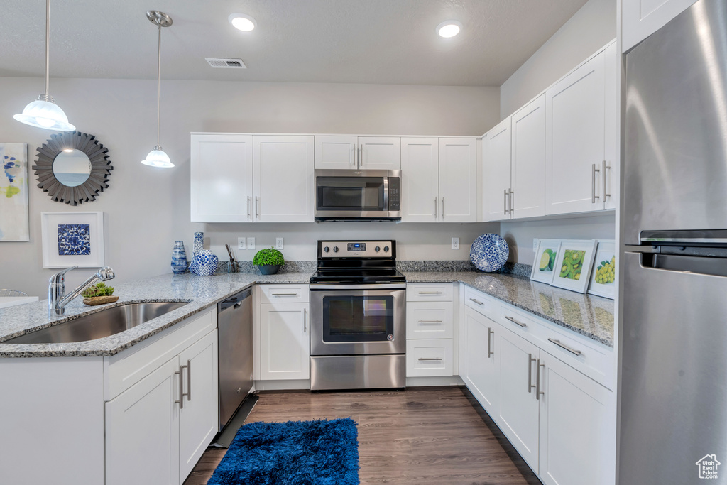 Kitchen with appliances with stainless steel finishes, white cabinetry, sink, and decorative light fixtures