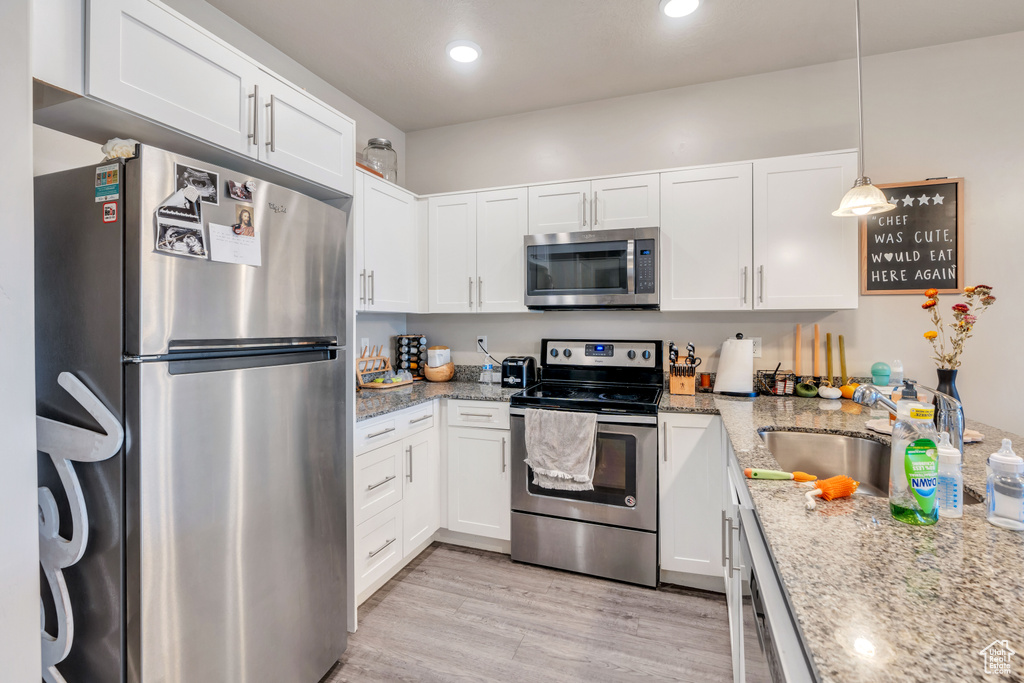 Kitchen with hanging light fixtures, white cabinetry, light stone counters, stainless steel appliances, and light wood-type flooring