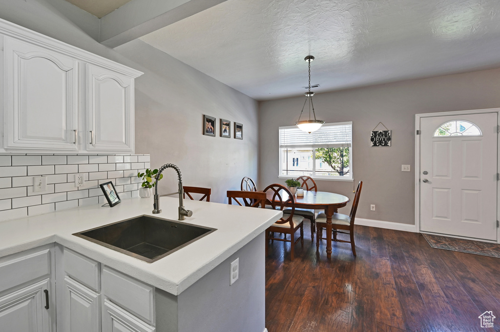 Kitchen featuring white cabinets, dark wood-type flooring, sink, hanging light fixtures, and backsplash