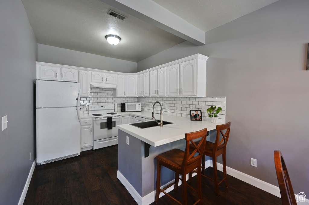 Kitchen featuring white cabinets, kitchen peninsula, sink, white appliances, and dark wood-type flooring