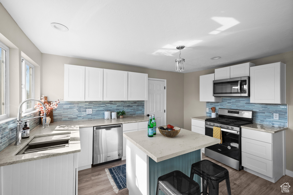 Kitchen featuring a kitchen island, stainless steel appliances, sink, white cabinetry, and light hardwood / wood-style flooring