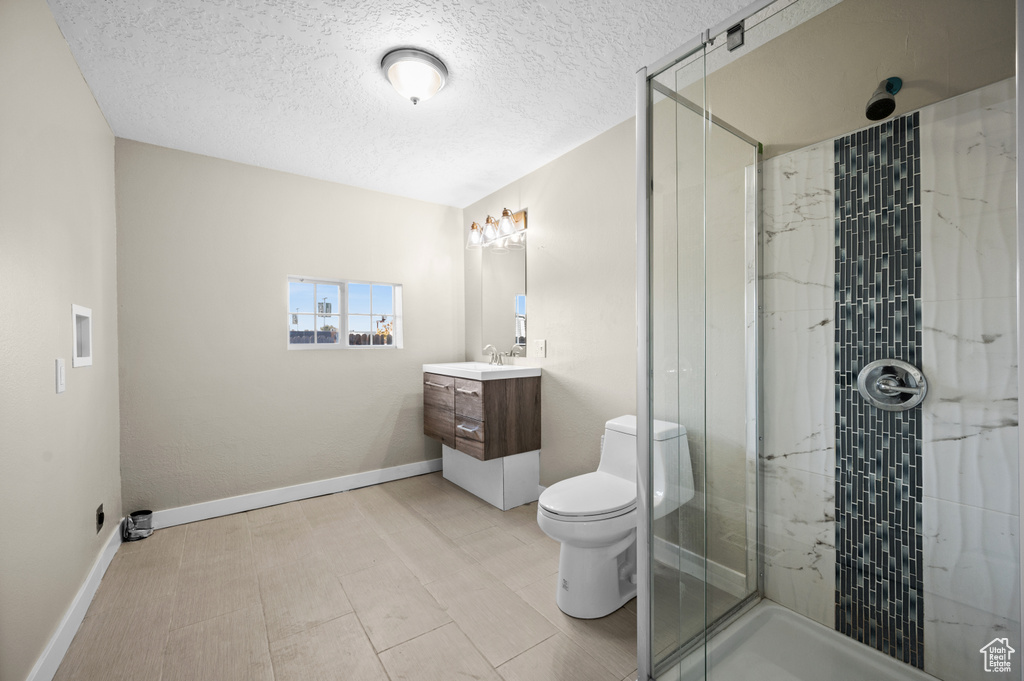 Bathroom featuring toilet, walk in shower, vanity, and a textured ceiling