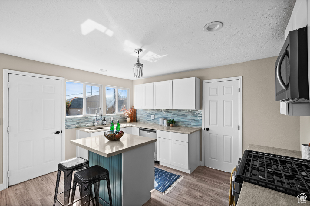 Kitchen featuring a center island, white cabinetry, stainless steel appliances, a breakfast bar, and light hardwood / wood-style floors