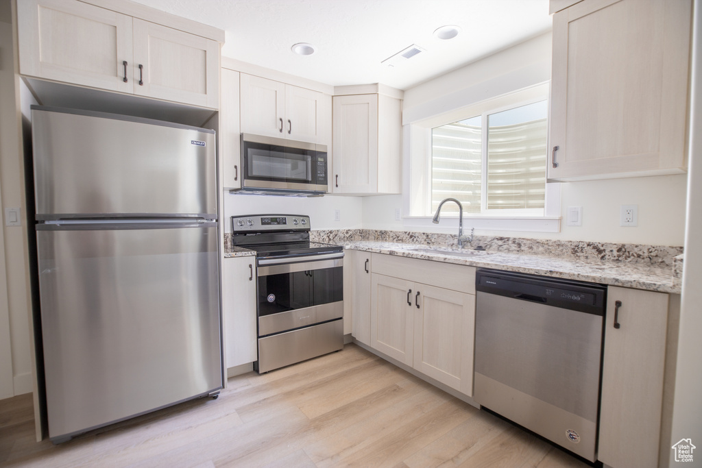 Kitchen with appliances with stainless steel finishes, light wood-type flooring, sink, and white cabinetry