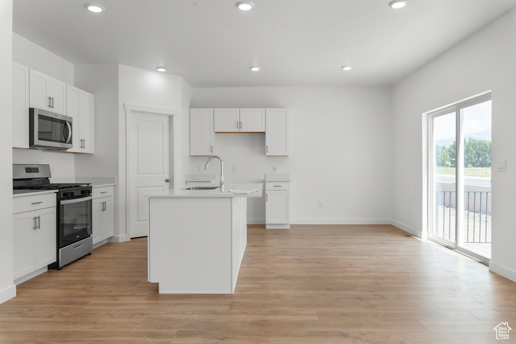 Kitchen featuring stainless steel appliances, sink, white cabinetry, light hardwood / wood-style flooring, and a center island with sink