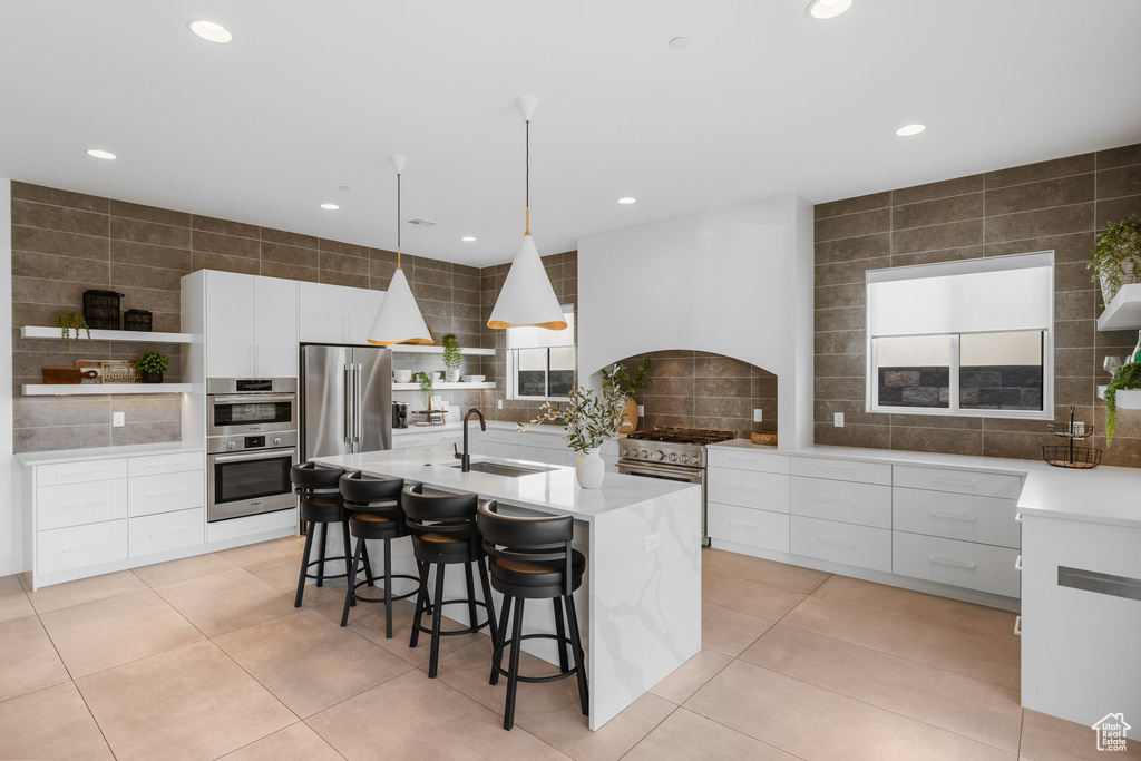 Kitchen featuring a kitchen island with sink, white cabinets, sink, appliances with stainless steel finishes, and decorative light fixtures