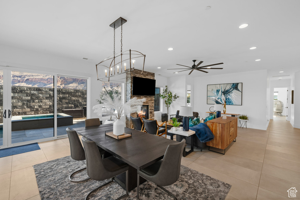 Tiled dining space with ceiling fan with notable chandelier, a fireplace, and a healthy amount of sunlight