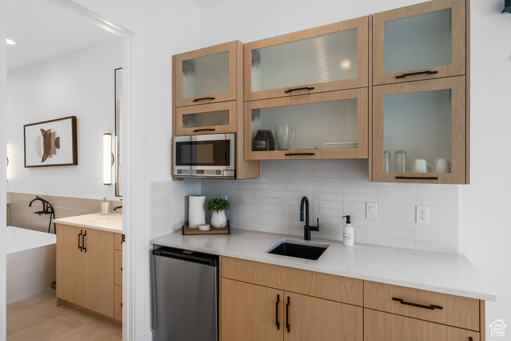 Kitchen with stainless steel appliances, backsplash, light brown cabinets, and sink